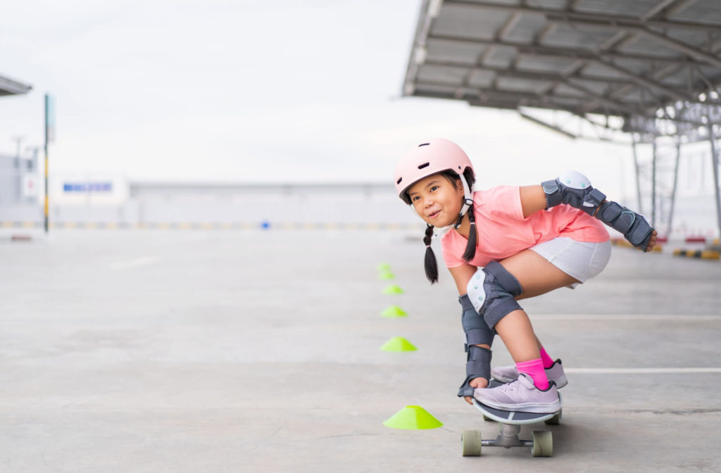 A young girl is riding a skateboard and wearing a safety  helmet, and elbow and knee pads for protection injury  and concussion.