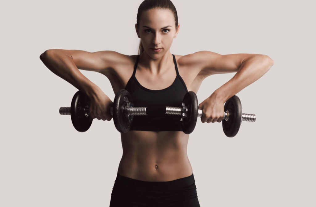 young woman in workout gear lifting dumbbells doing upright row exercises which can cause shoulder impingement.