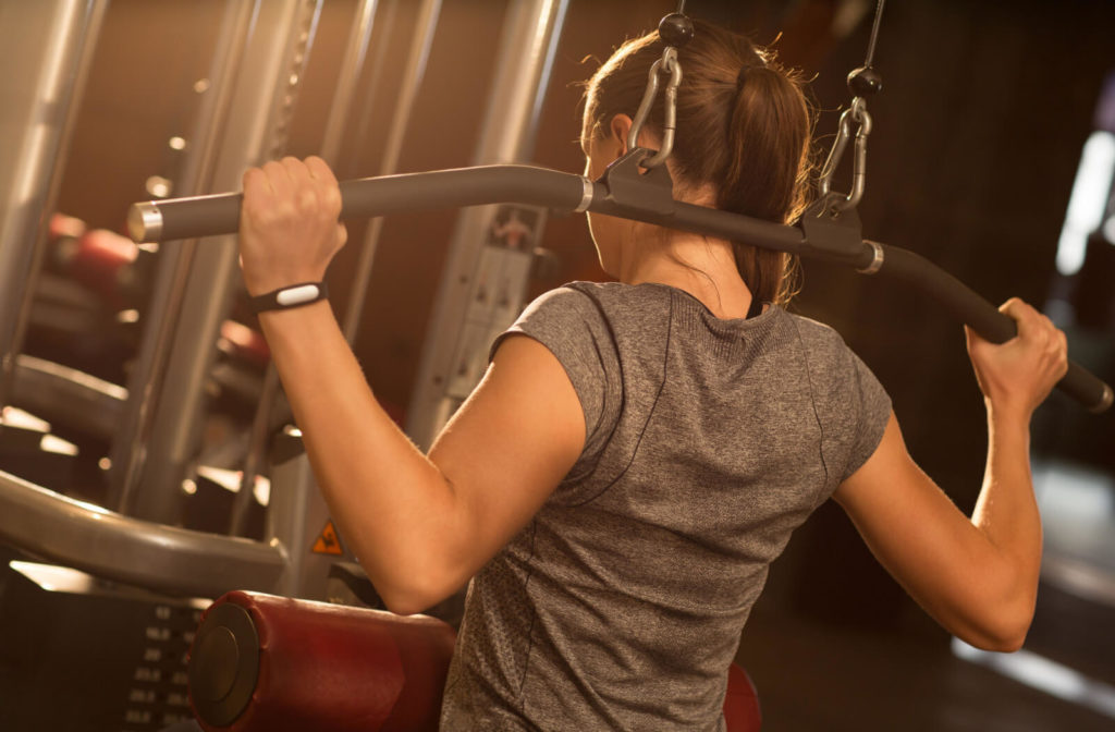 A young woman is exercising at the gym doing lat pulldown machine.Pulling the lat pulldown bar behind your head is a bad idea for healthy shoulders