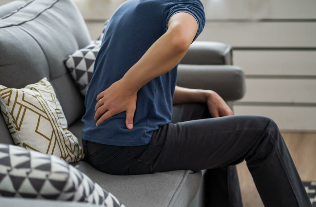 A man suffering from back pain at home The man is touching his back while sitting on a sofa