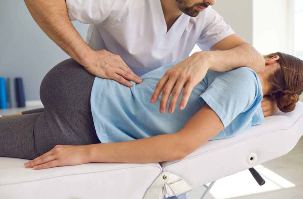 "A male chiropractor helping treat a patient's pinched nerve as they lie on their back on a reclined medical chair with their hips rotated to the side."