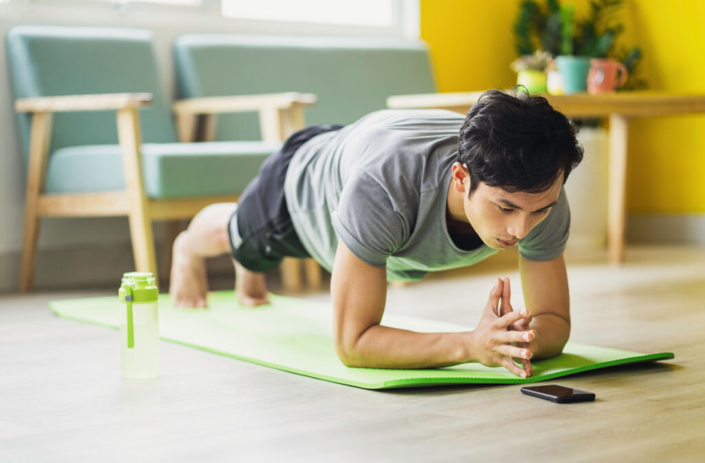 An athletic young man planking on a green exercise mat.
