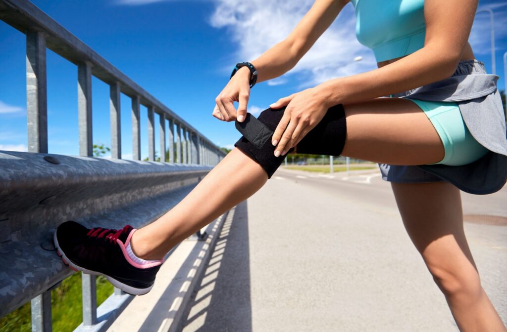 An athlete stops to adjust their knee brace to prevent injuries while running.