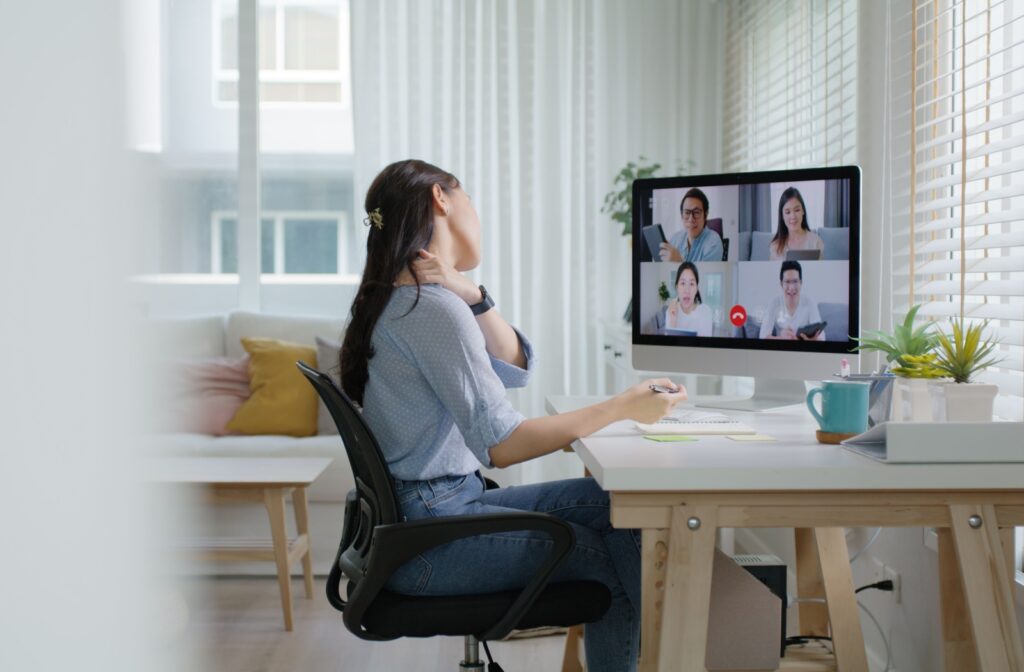 a person holding their neck during a workplace video chat meeting to relieve tech neck symptoms.