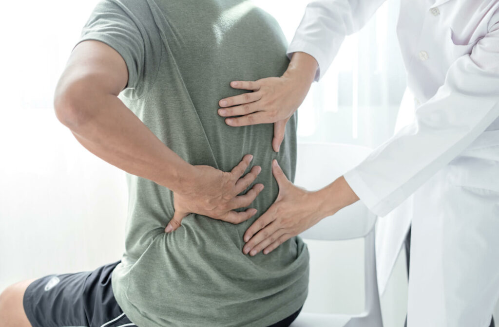 A patient rubbing their lower back while a physiotherapist checks their range of motion during a consultation.