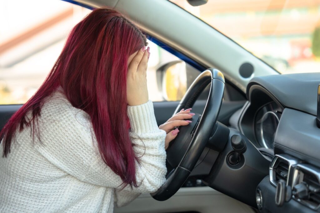 Person sitting in the drivers seat of a car holding their head